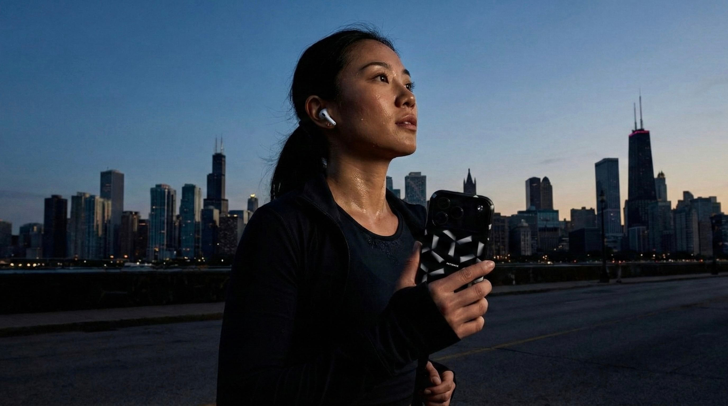 A woman running with the NYC skyline in the background. She listens to music and holds her iPhone with Aesmor case
